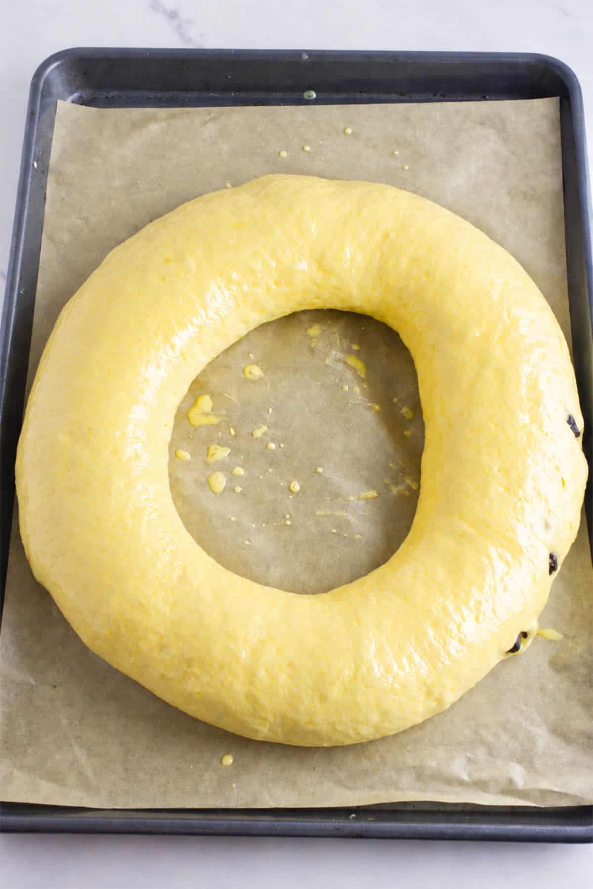 Rosca de Reyes wreath brushed with egg wash before adding cookie paste and candied fruit decorations.