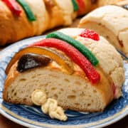 Close-up of Rosca de Reyes slice with candied fruit and cookie paste topping on a blue plate.