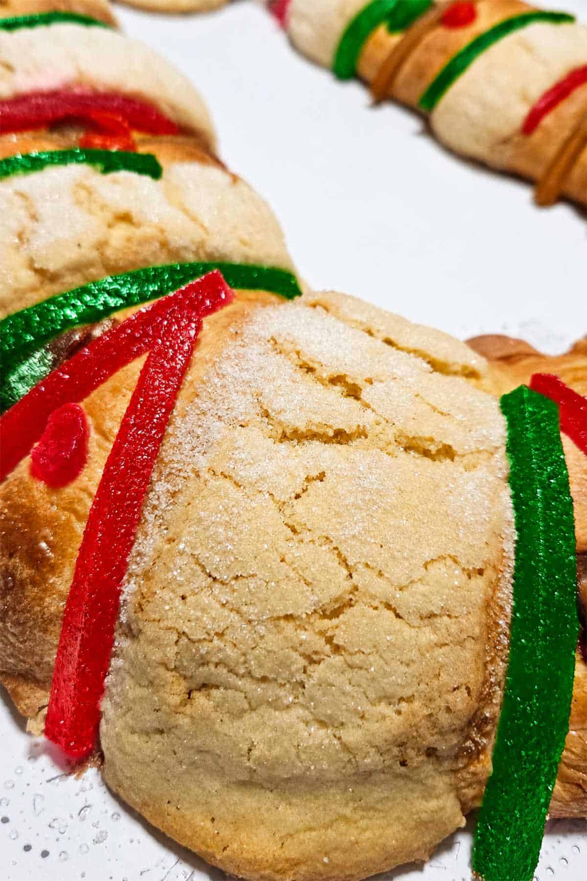 Golden Rosca de Reyes wreath with candied fruit, sliced almonds, and white icing.