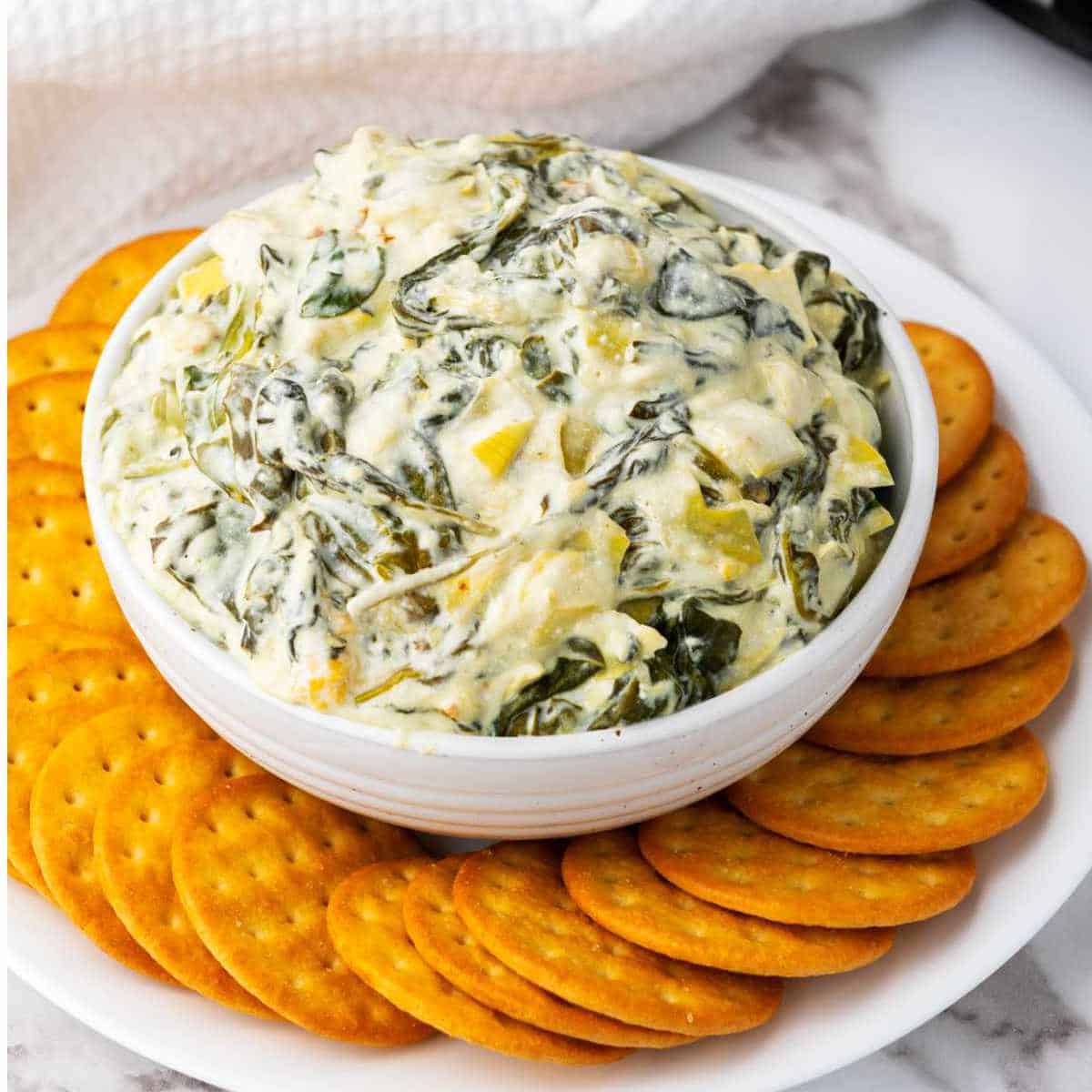 keto spinach artichoke dip in a bowl surrounded by crackers.