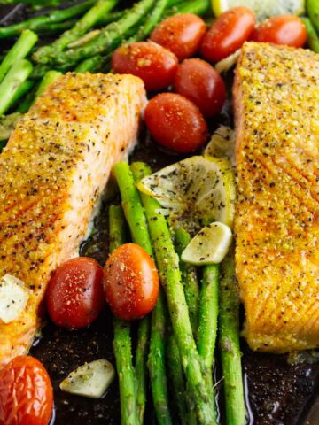 baking tray with roasted seasoned asparagus spears, sliced lemons, blistered tomatoes, and broiled Coho salmon.
