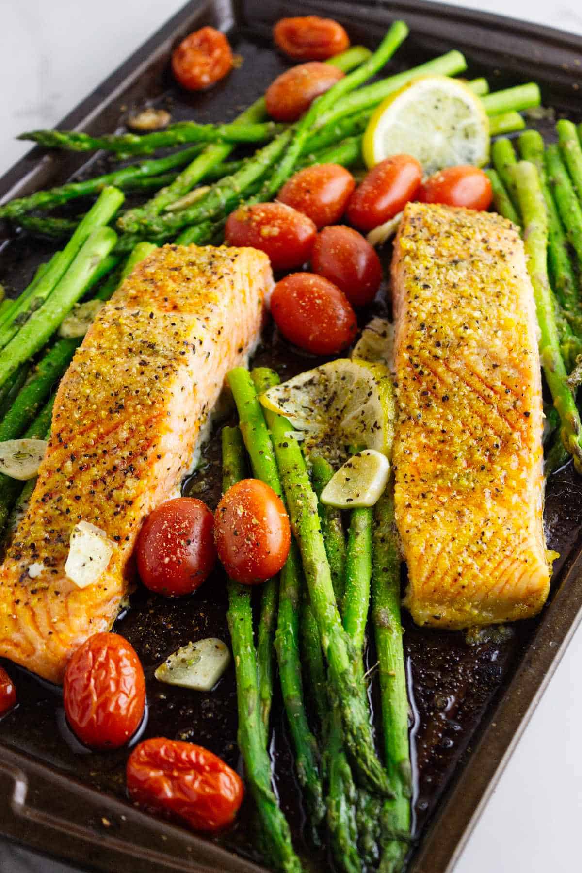 baking tray with roasted seasoned asparagus spears, sliced lemons, blistered tomatoes, and broiled Coho salmon.