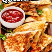 Steak quesadilla wedges with melted cheese and herbs, served on a white plate with sour cream.