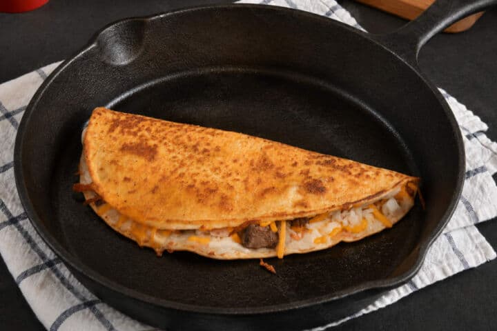 Folded steak quesadilla cooking in a cast iron skillet.