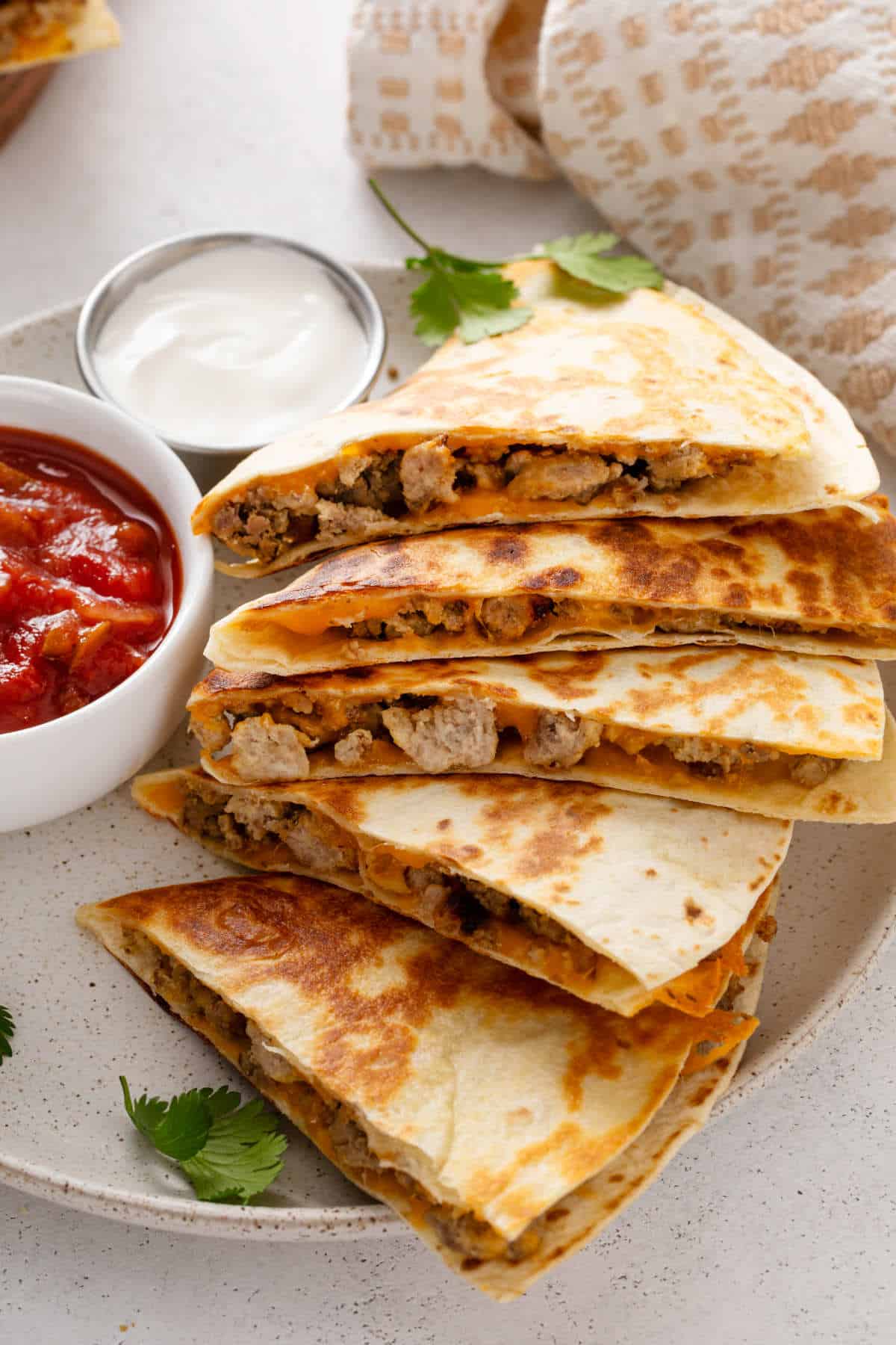Cheesy steak quesadilla wedges on a white plate with sour cream.