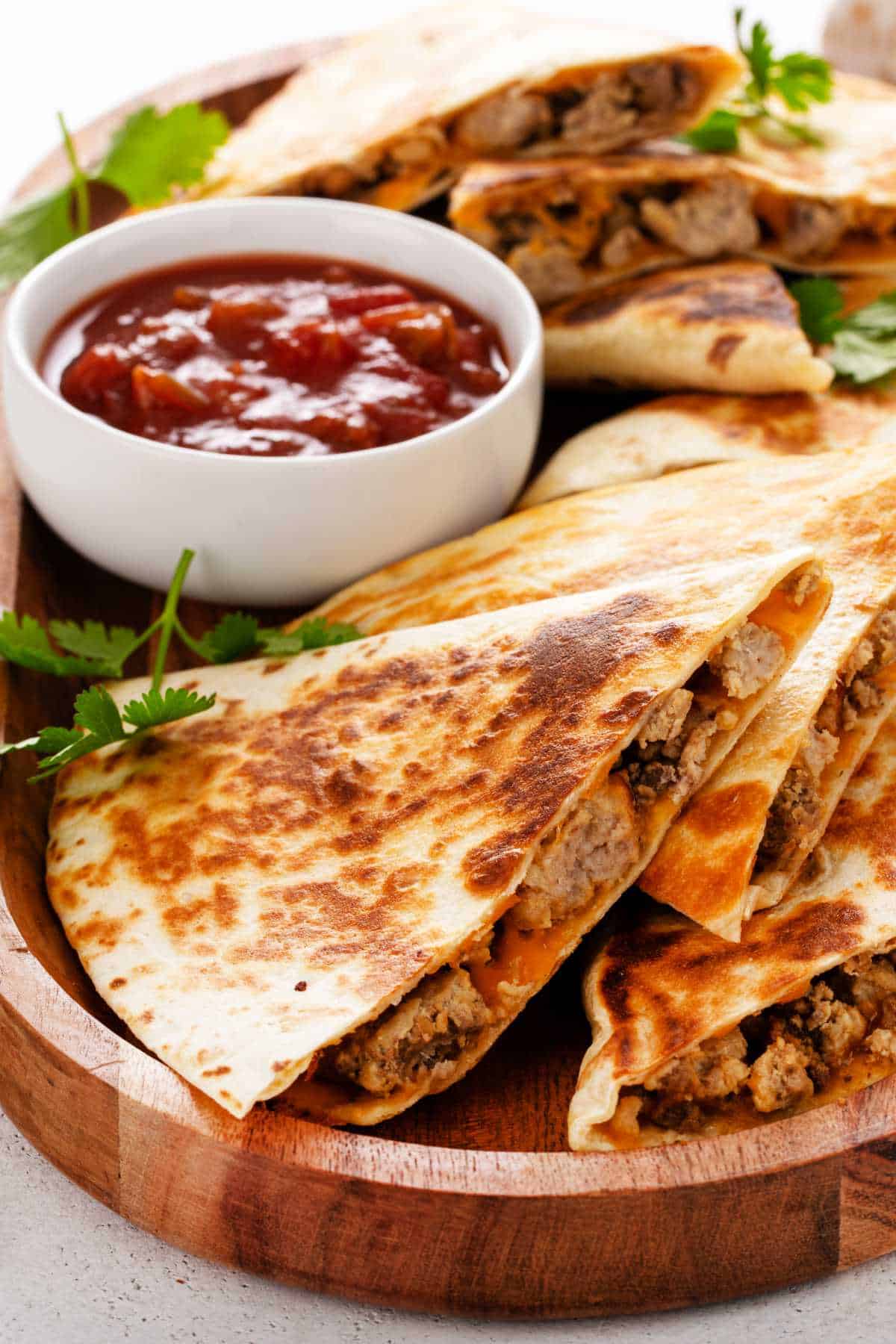Steak quesadilla wedges stacked on marble with melted cheese and fresh herb garnish.