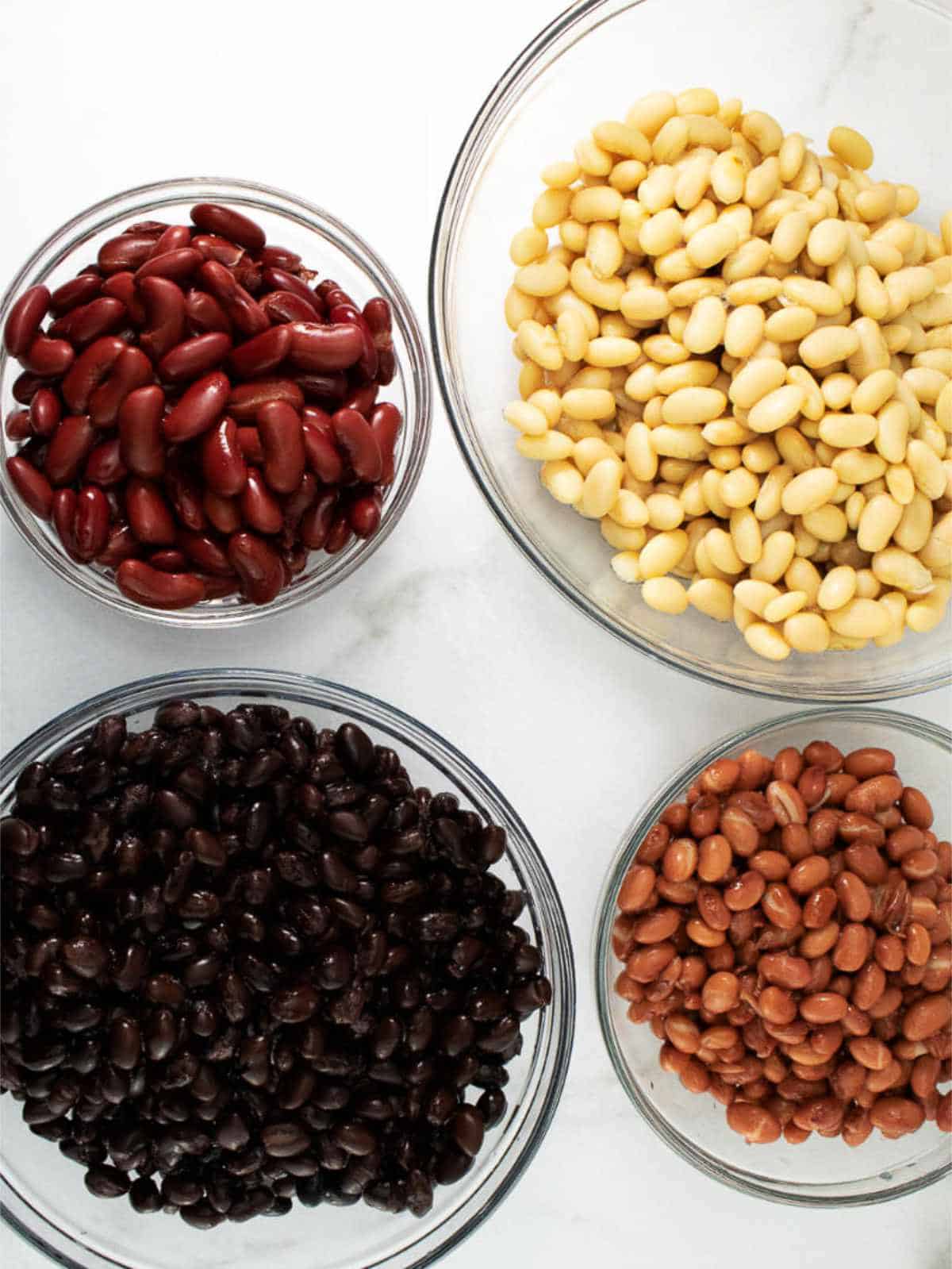 clear glass bowls of pinto beans, navy beans, black beans, and kidney beans.
