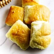 A basket filled with fluffy, golden-brown dinner rolls sits on a white surface.