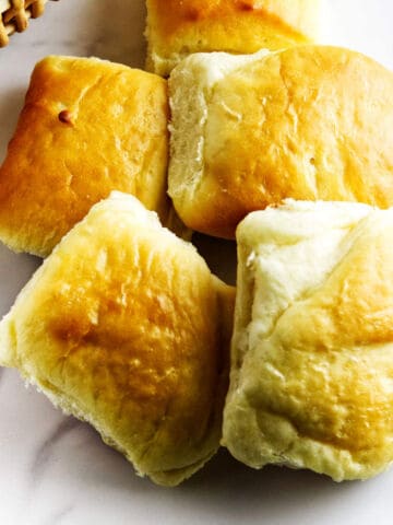 A basket filled with fluffy, golden-brown dinner rolls sits on a white surface.