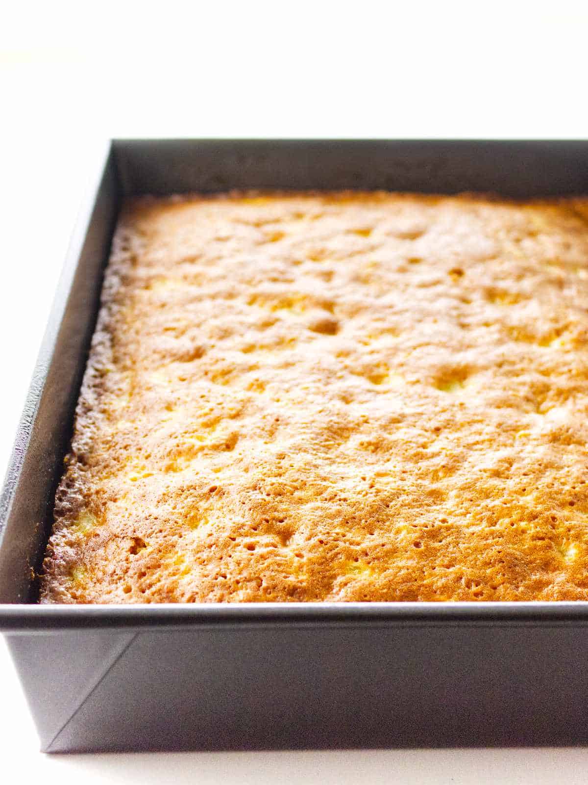 A freshly baked texas tornado cake in a square metal baking pan, with a golden brown, slightly textured surface.