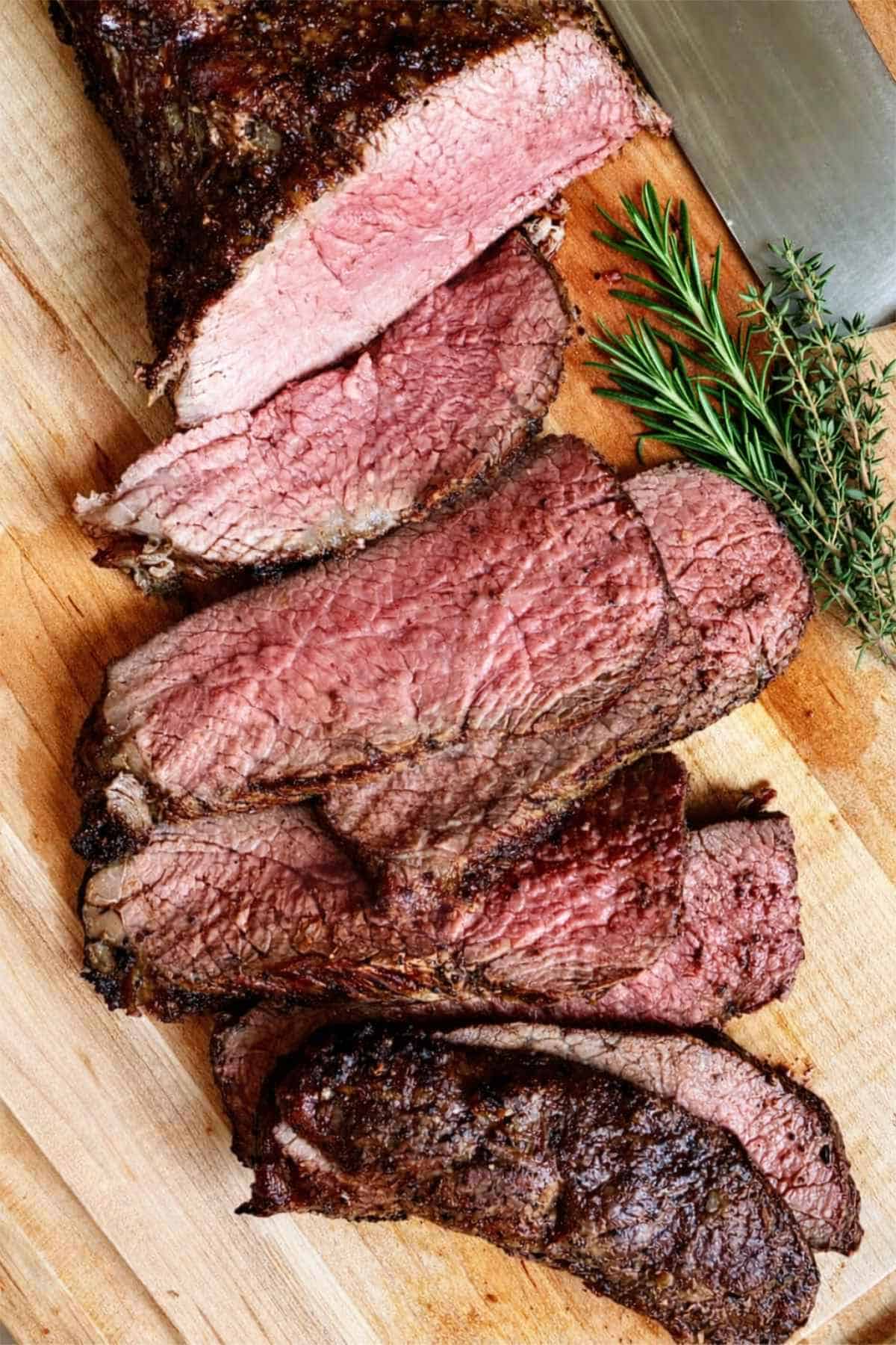 Sliced oven roasted tri tip arranged on a white oval plate with a pink, juicy center and seasoned crust.