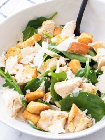 Bowl of Caesar salad with air fried chicken breast with croutons and shaved Parmesan cheese.