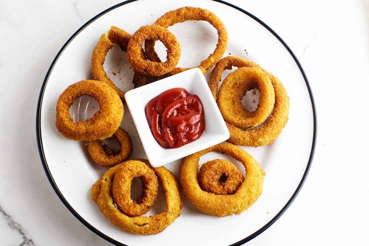 golden brown breaded onions on a plate with a sauce bowl of ketchup.