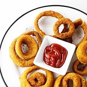golden brown breaded onions on a plate with a sauce bowl of ketchup.
