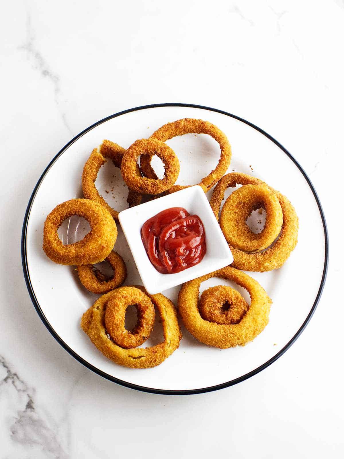 golden browned air fryer onion rings on a plate with a sauce bowl of ketchup.