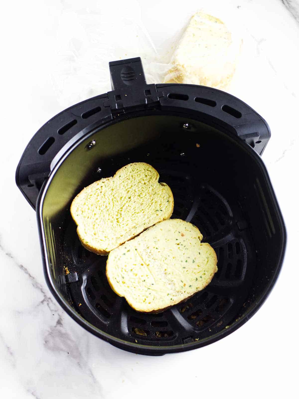 frozen buttered Texas Toast spread out in an airfryer basket.