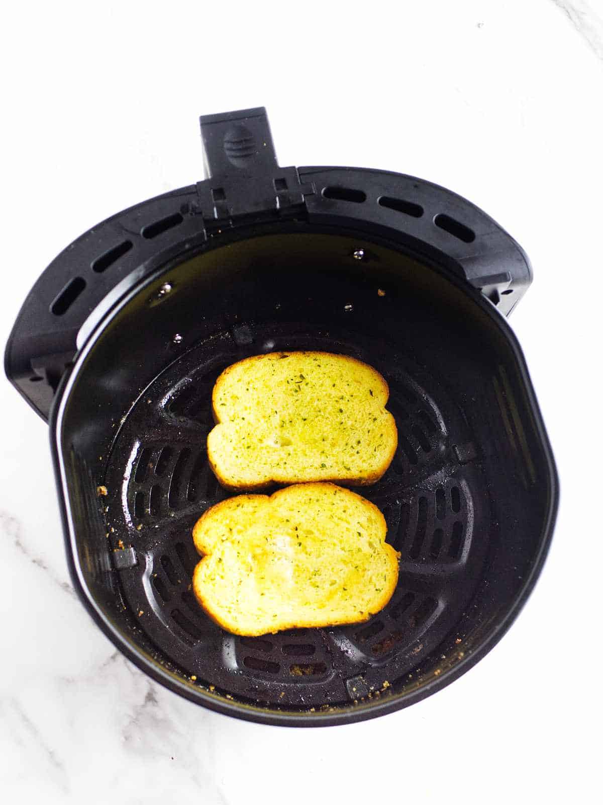 toasted French bread with garlic butter and herb in an airfryer basket.