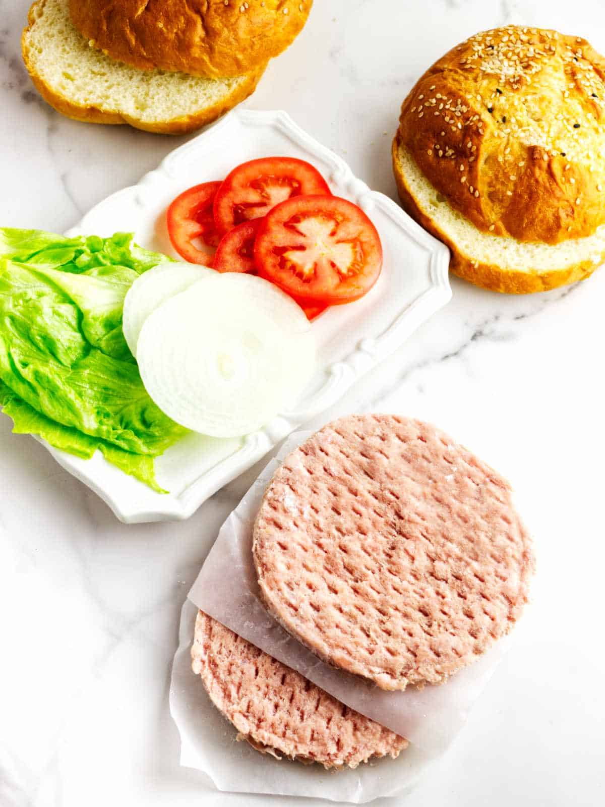 frozen turkey burgers, buns, and fixings on a white marble counter.
