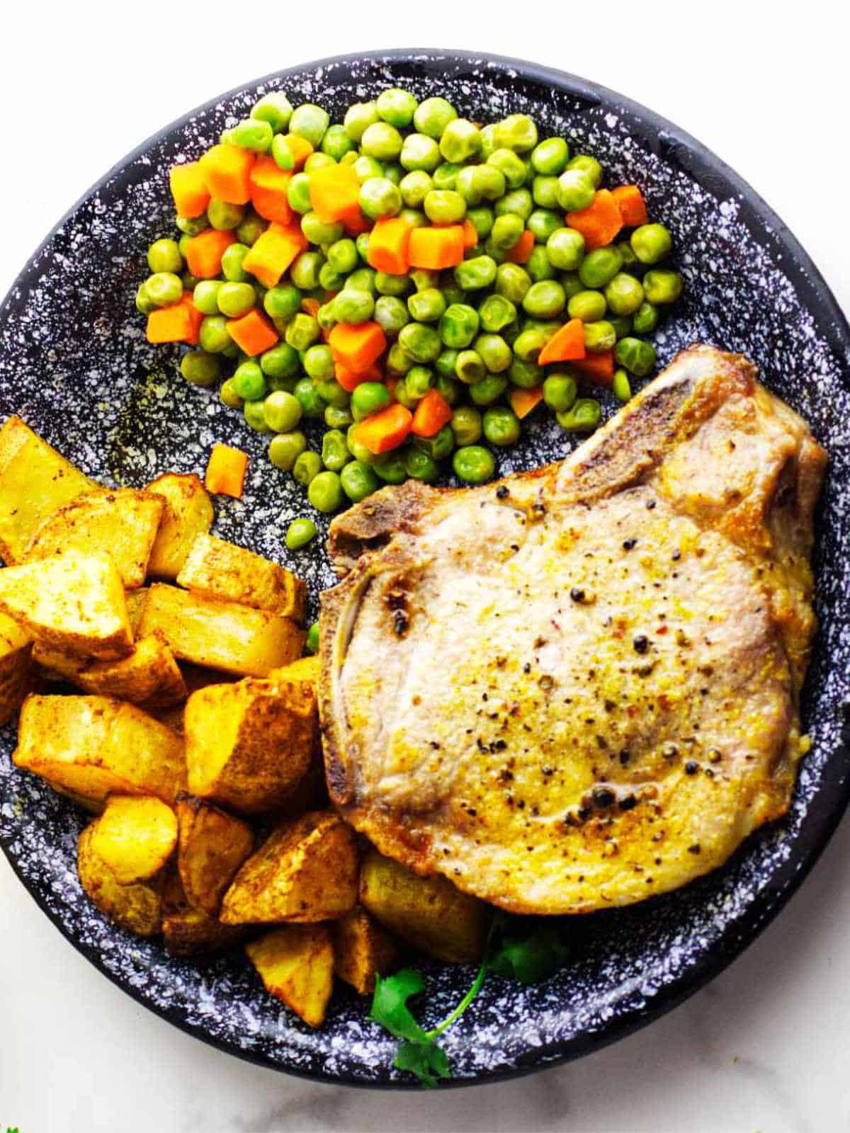 seasoned pork chops (no breading), on a plate with peas and carrots and diced potatoes.