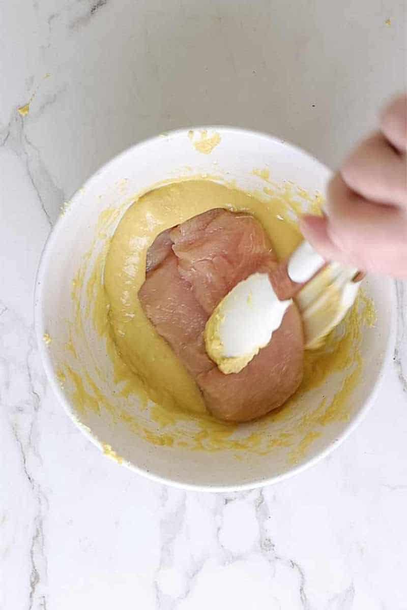 coating chicken breast in mustard and egg mixture.