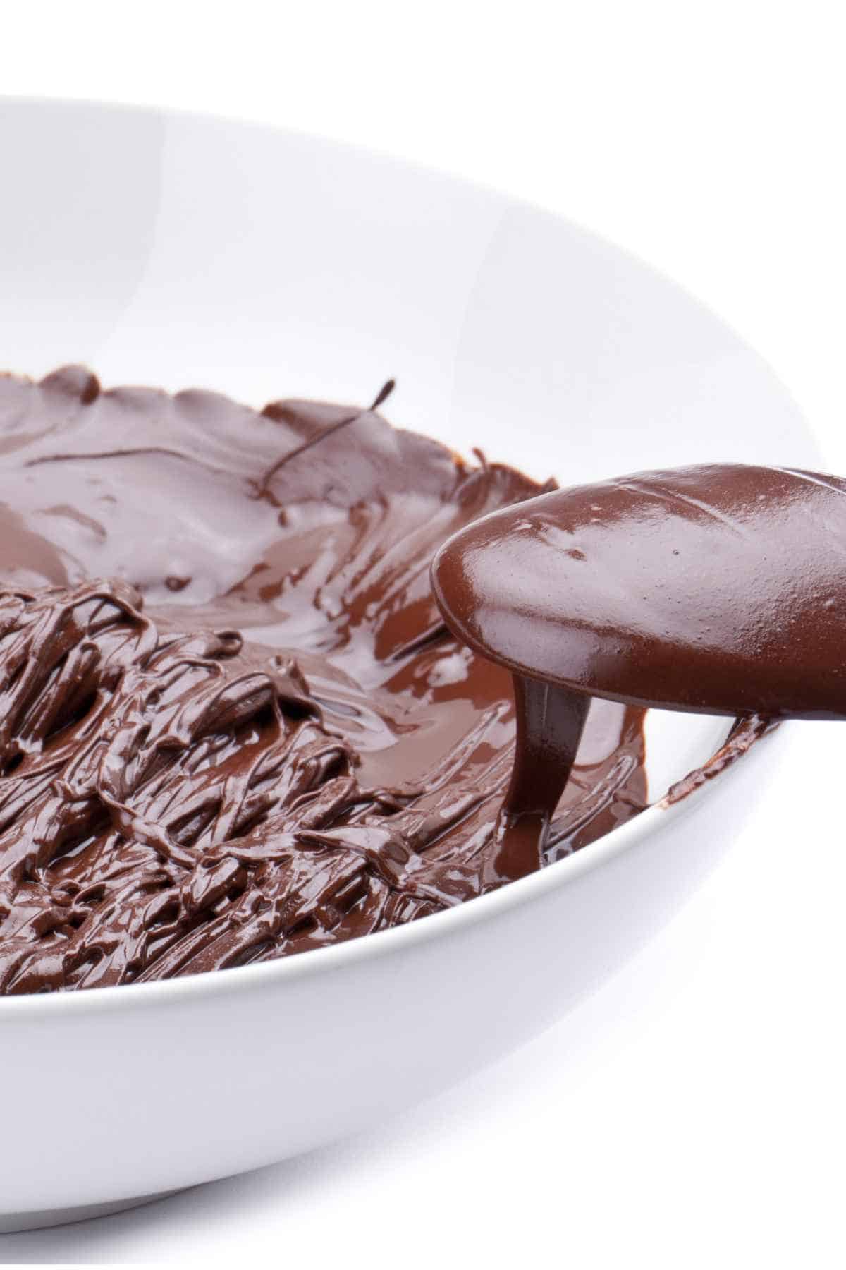 A bowl of chocolate sauce with spoon on a white background.
