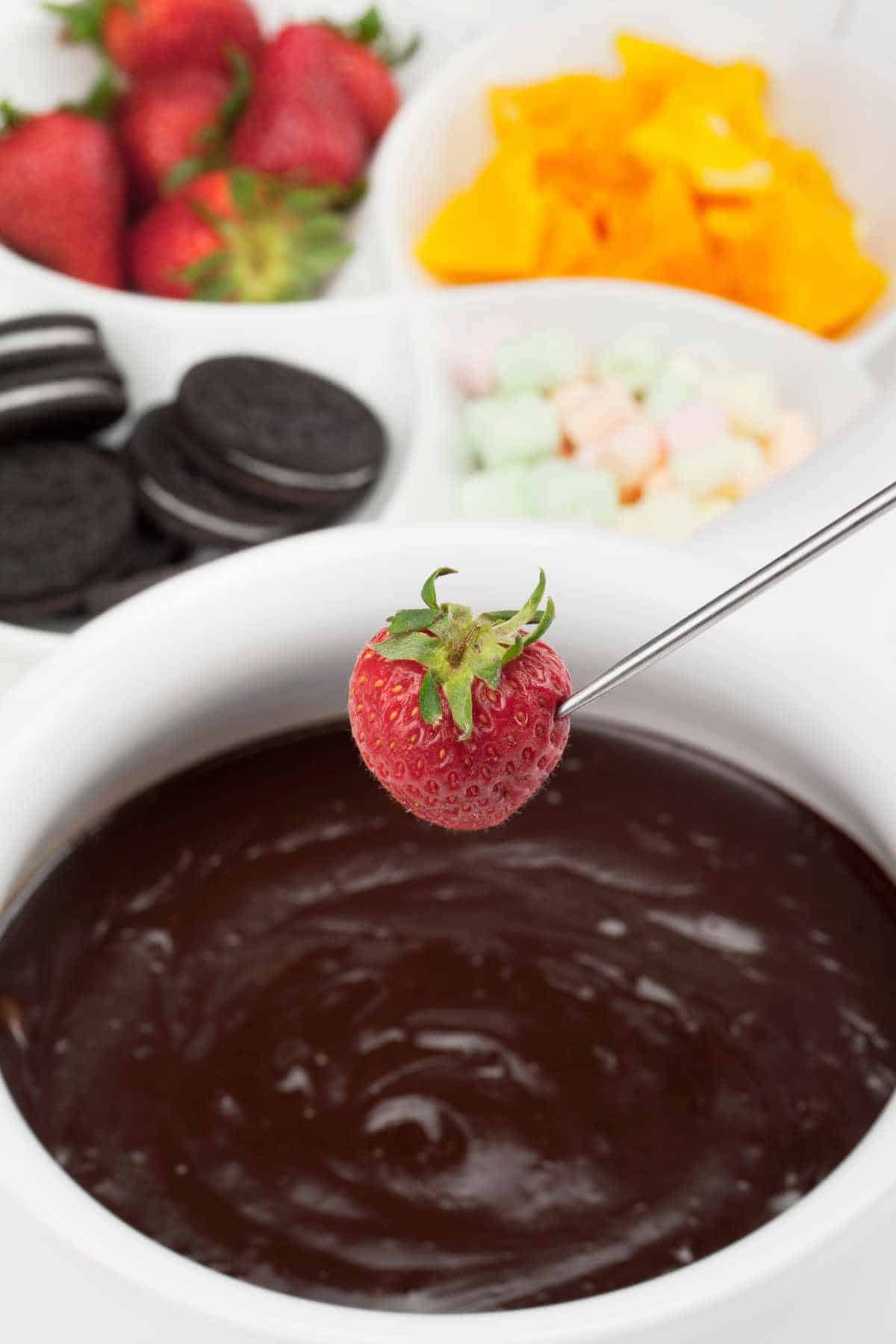 Close up image of strawberry and melted pot of chocolate sauce.