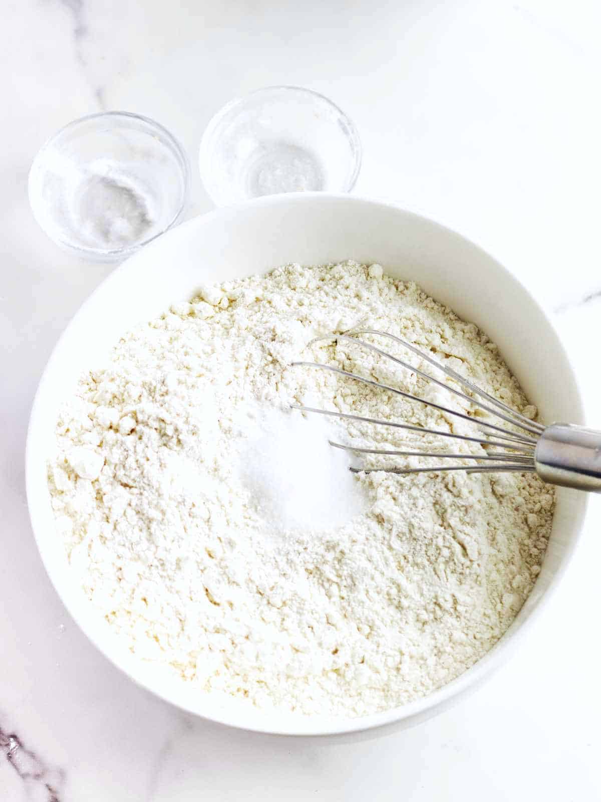 whisk in a bowl of dry ingredients on a white marble backgrounds.