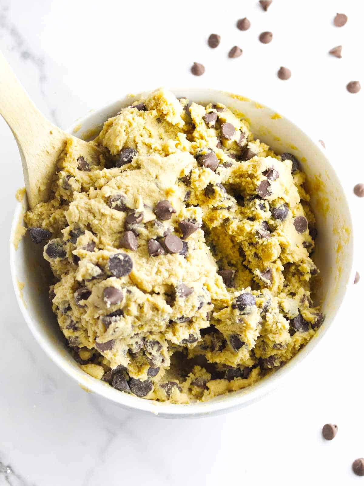 chocolate chips mixed into cookie dough in a large bowl on a white marble background.