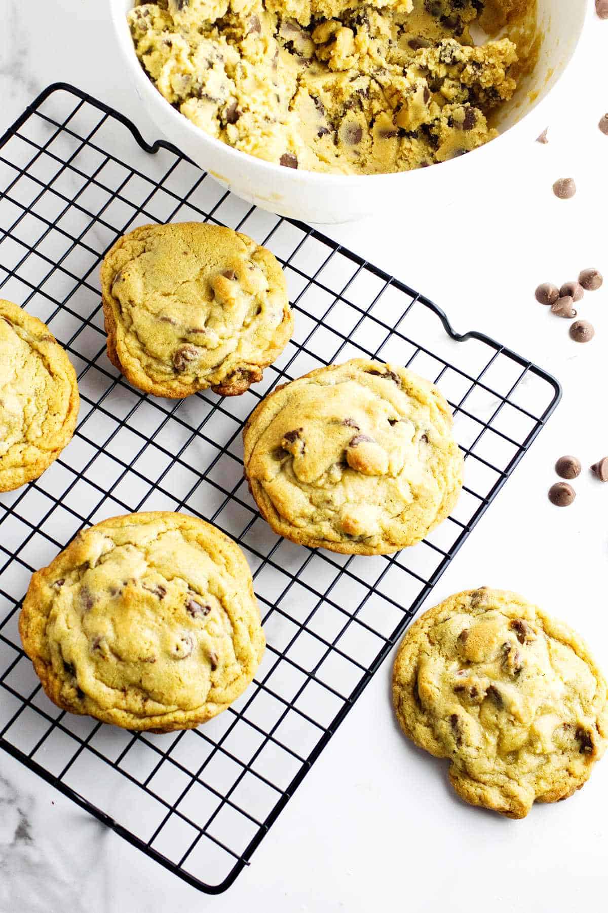 large bakery style chocolate chip cookies on a cooling rack against a white marble background.