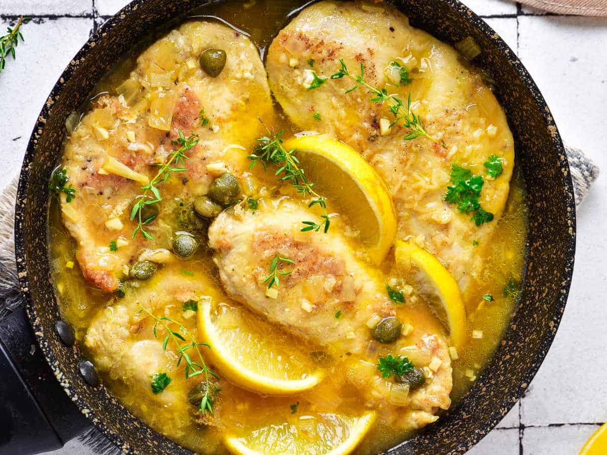 cast iron skillet with chicken breasts and lemon slices.