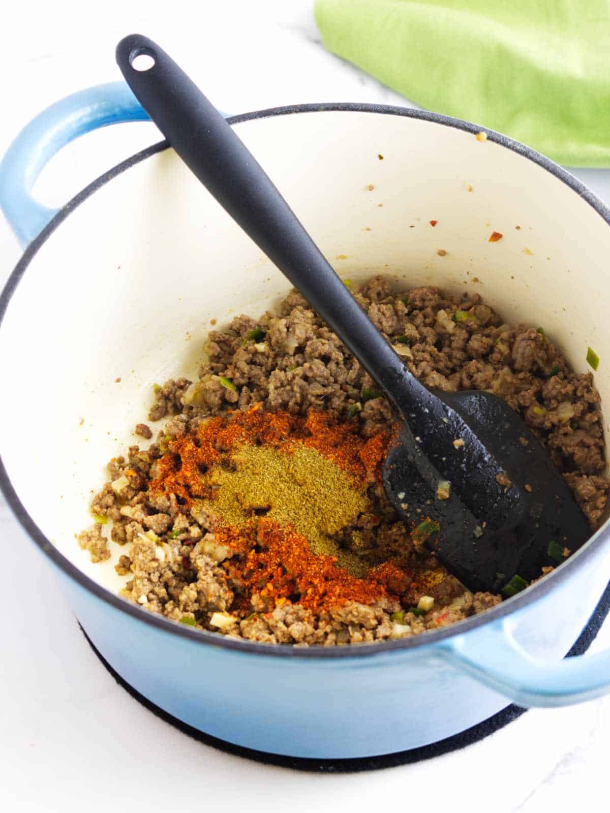 spices added to ground beef in an enameled dutch oven.