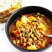 ground beef cowboy soup in a bowl with bread nearby.