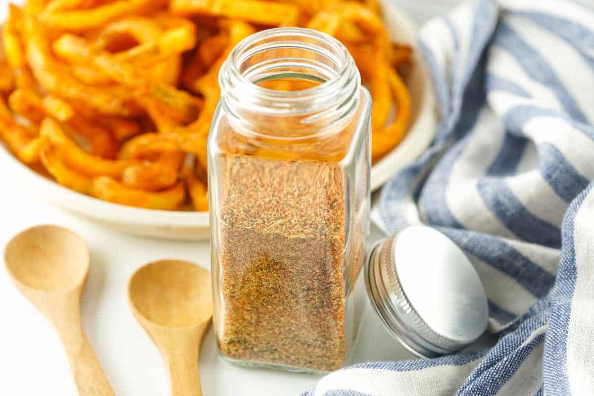 jar of homemade fry seasoning with seasoned curly fries in the background.