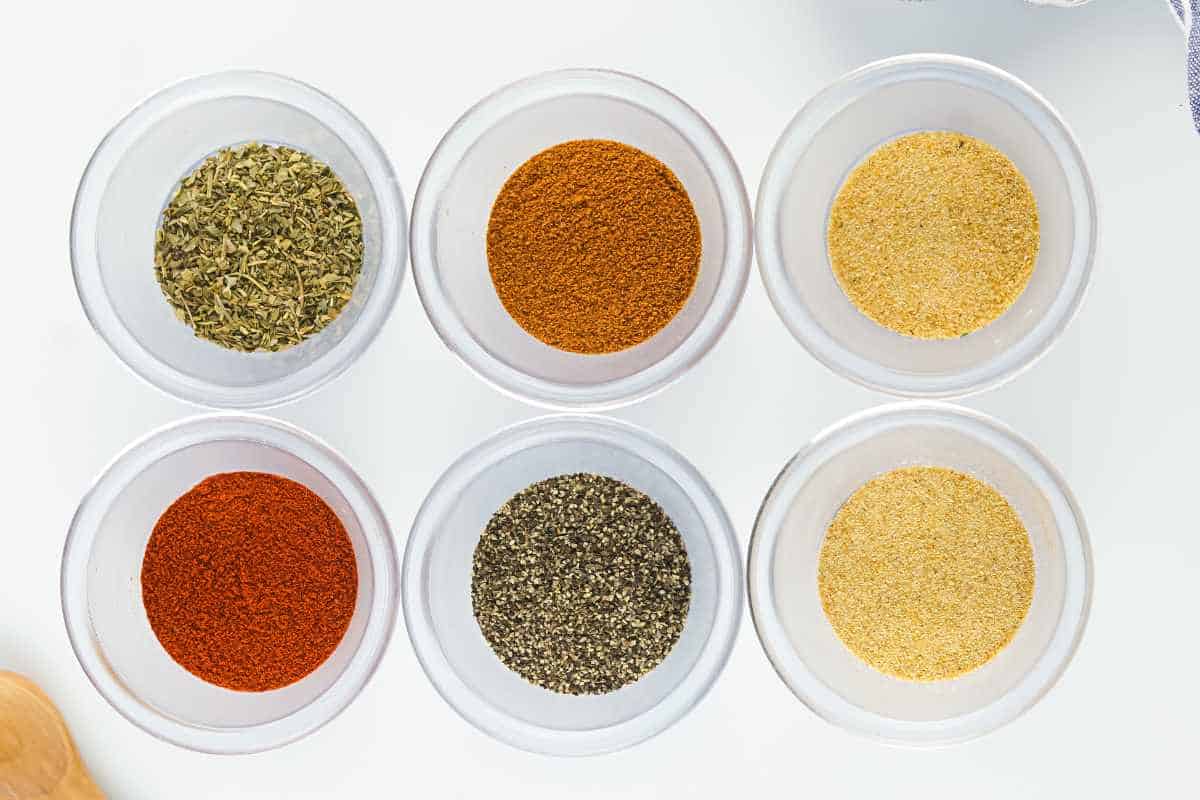 various colorful spices in individual bowls on a white background.