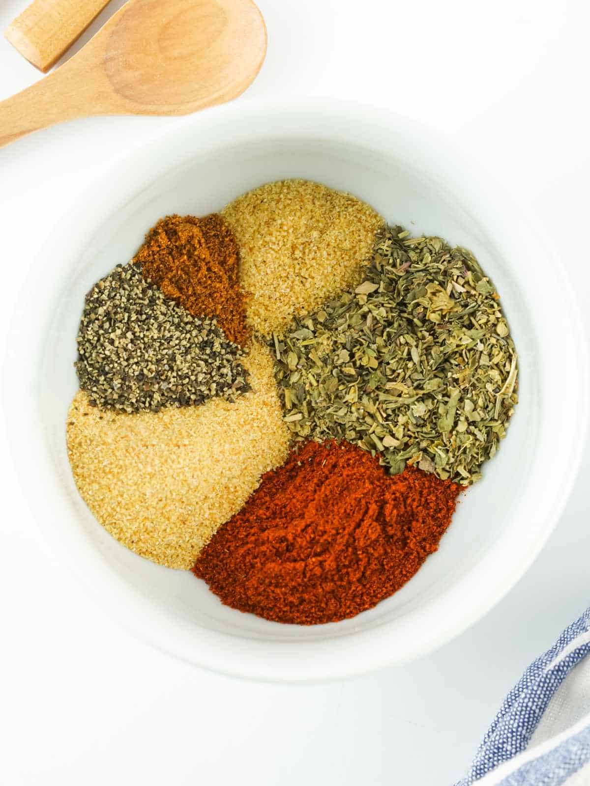 various colorful spices sectioned in a white bowl on a white background.