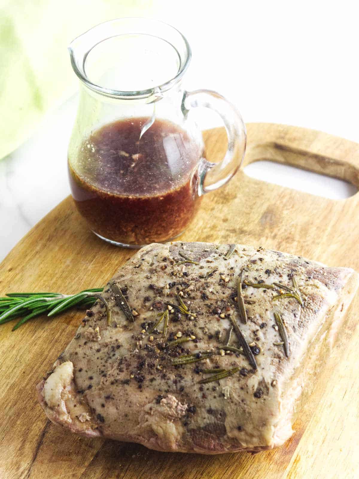 cooked meat resting on a cutting board with au jus in a small pitcher nearby.