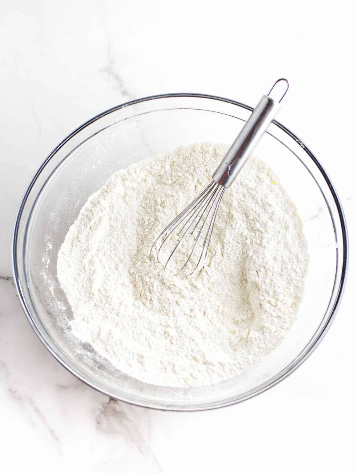 dry ingredients in a bowl with a whisk on a white marble background.