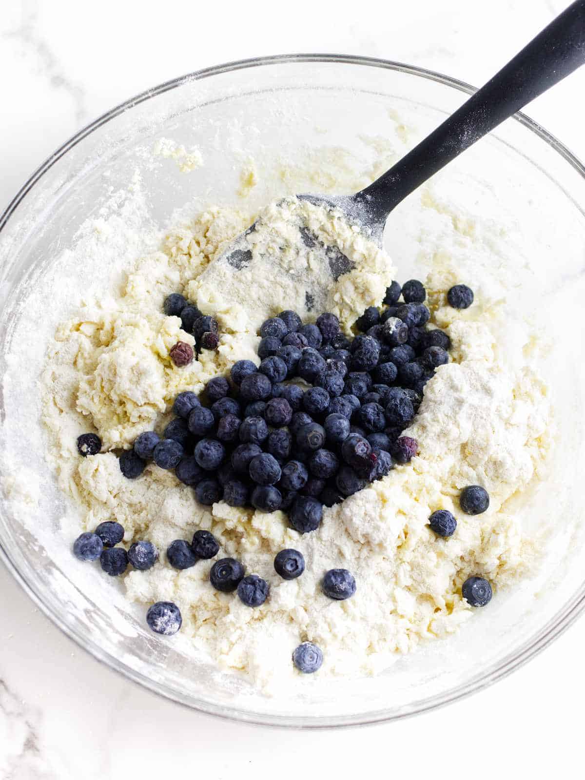 clear glass bowl of dough mixed with fresh blueberries.