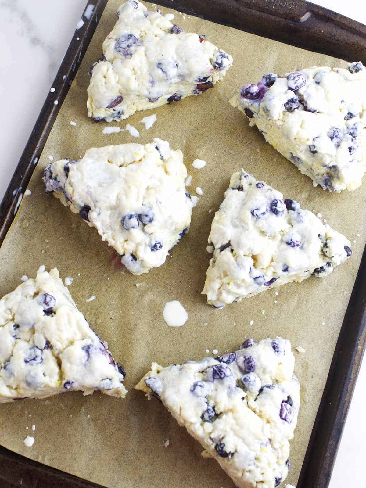 wedge shaped blueberry scones on a parchment paper lined baking sheet.