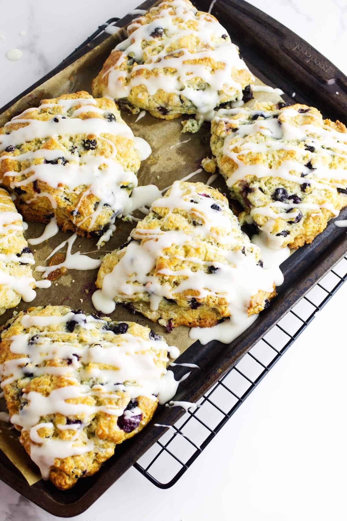 Icing drizzled over copycat starbucks blueberry scones on a baking sheet.