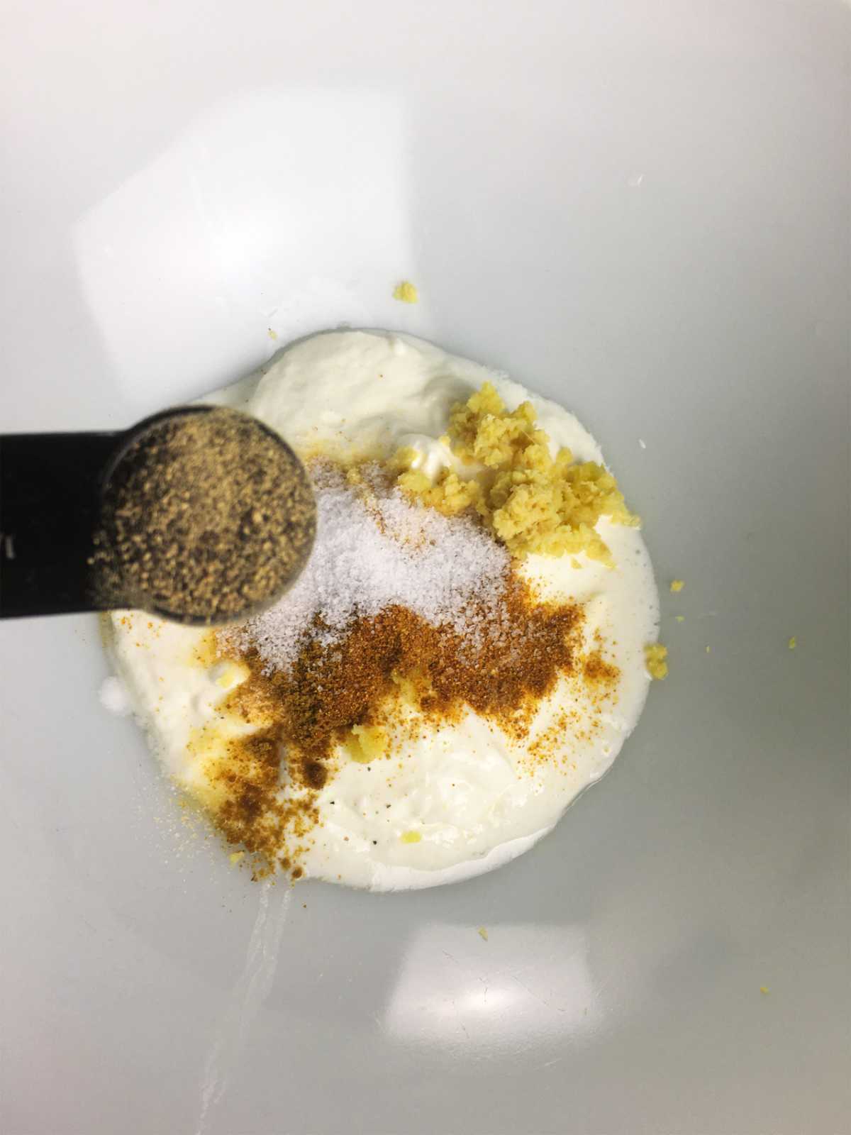 spices added to yogurt in a white glass bowl.