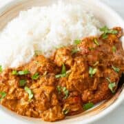 chicken tikka masala with rice, garnished with cilantro in clay serving bowl.
