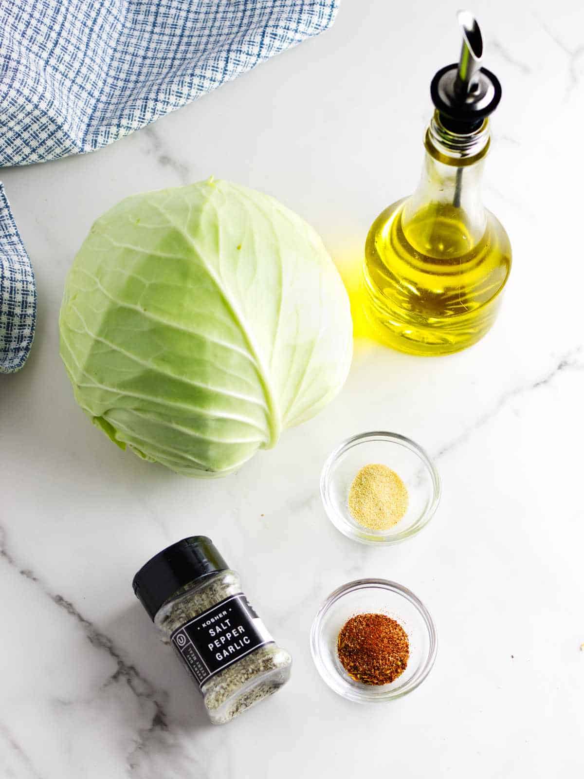 head of cabbage, oil, and garlic powder on a white marble background.