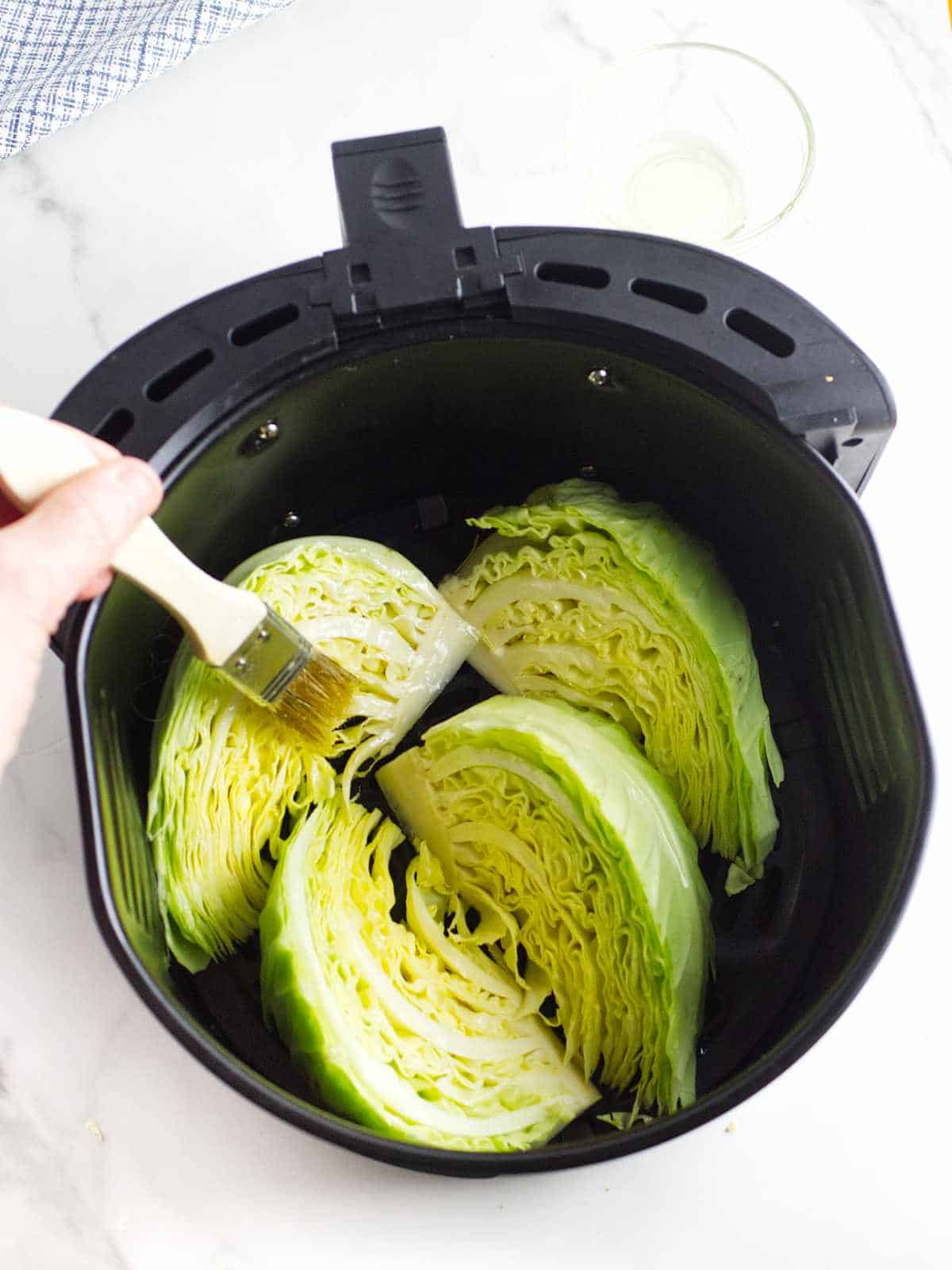 brushing olive oil on cabbage wedges in an air fryer basket.
