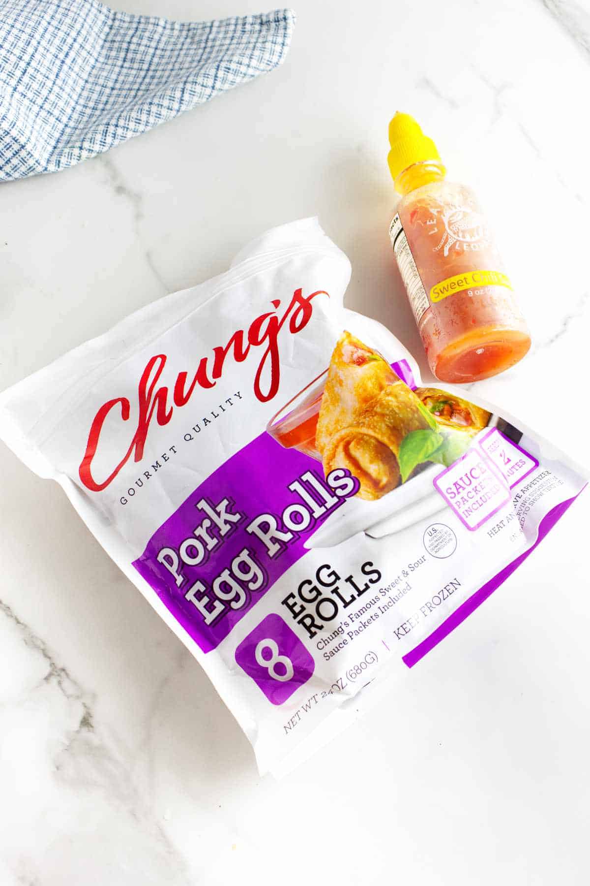 bag of frozen egg rolls in air fryer and some sweet chili sauce on a white background.