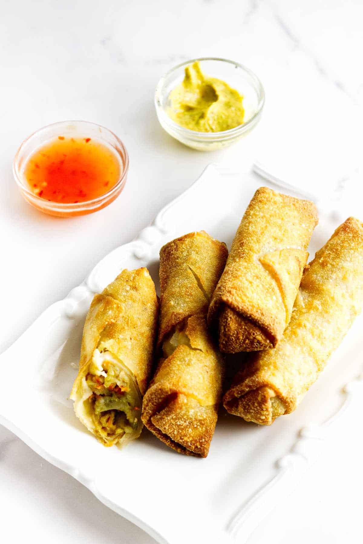 serving plate with four golden brown frozen egg rolls in air fryer with chili sauce on the side.