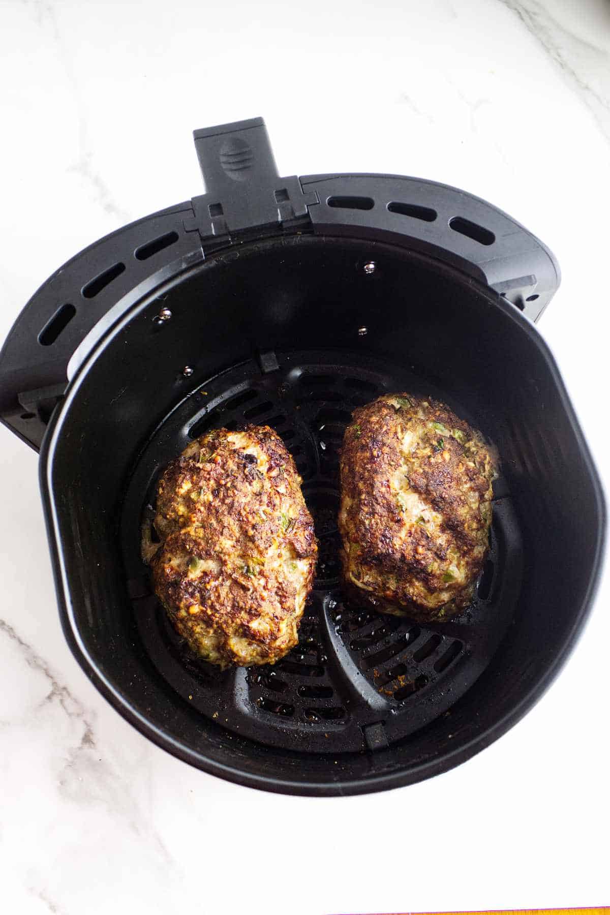 two small cooked meatloaves in an air fryer basket.