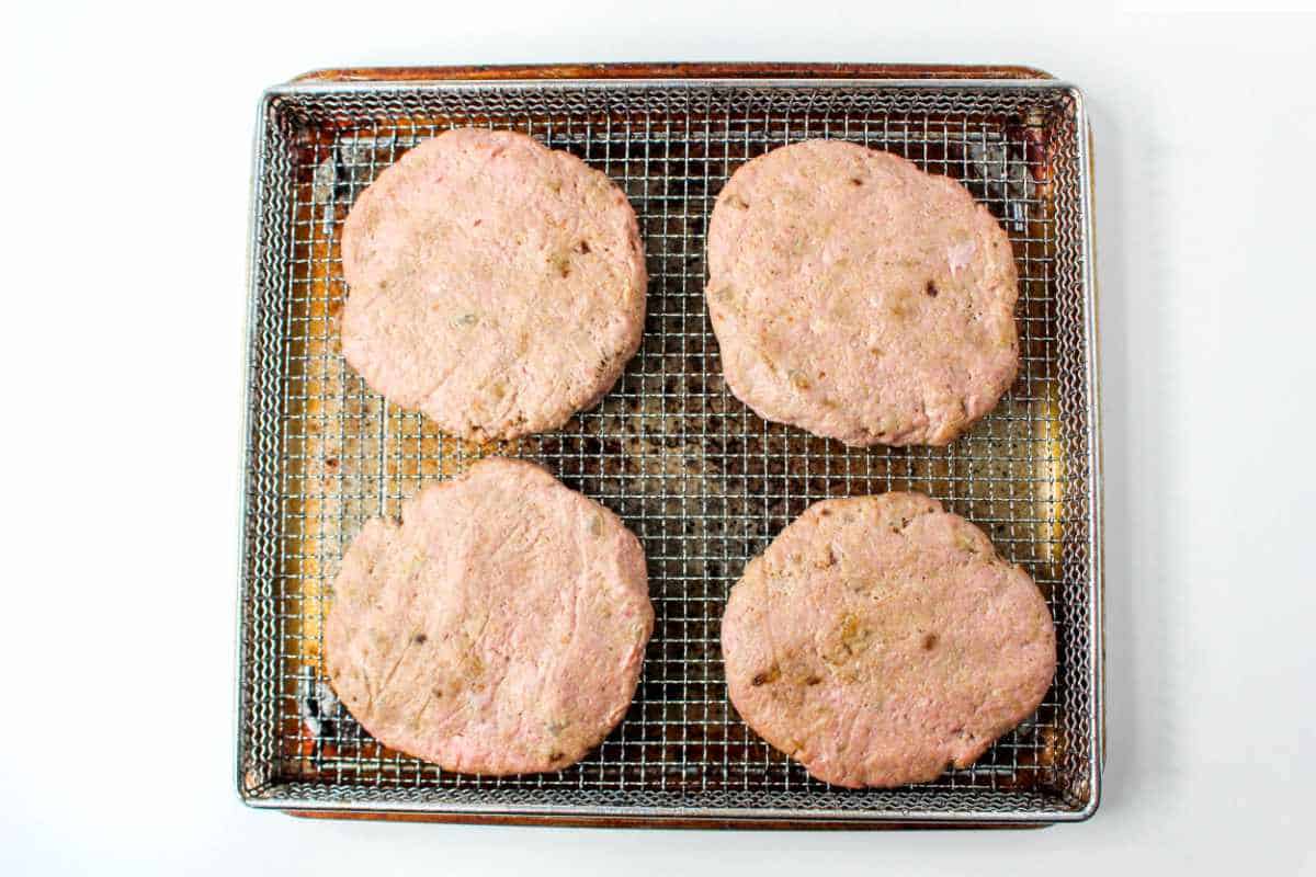 raw turkey burger mixture shaped into four patties on an air fryer rack on top of a slide in air fryer pan.