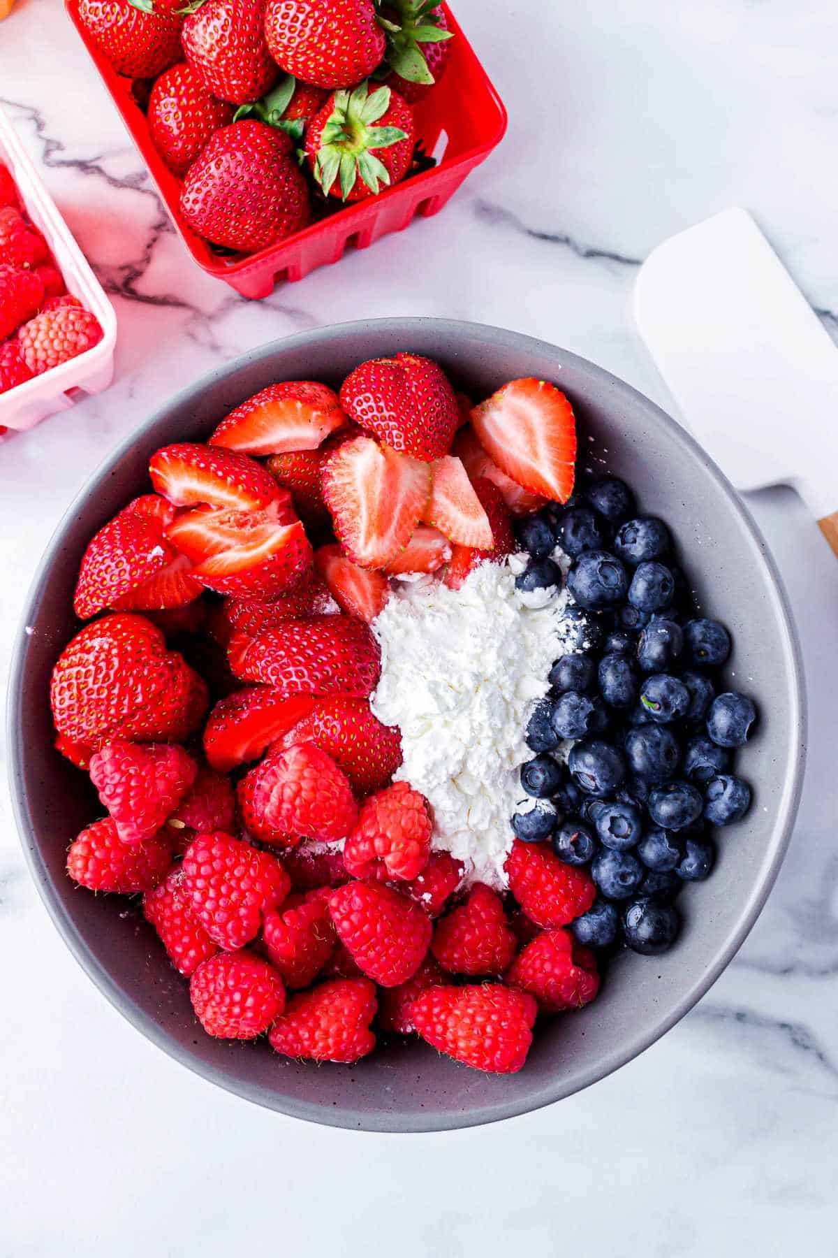 strawberries, blueberries, and raspberries in a bowl with some sugar.