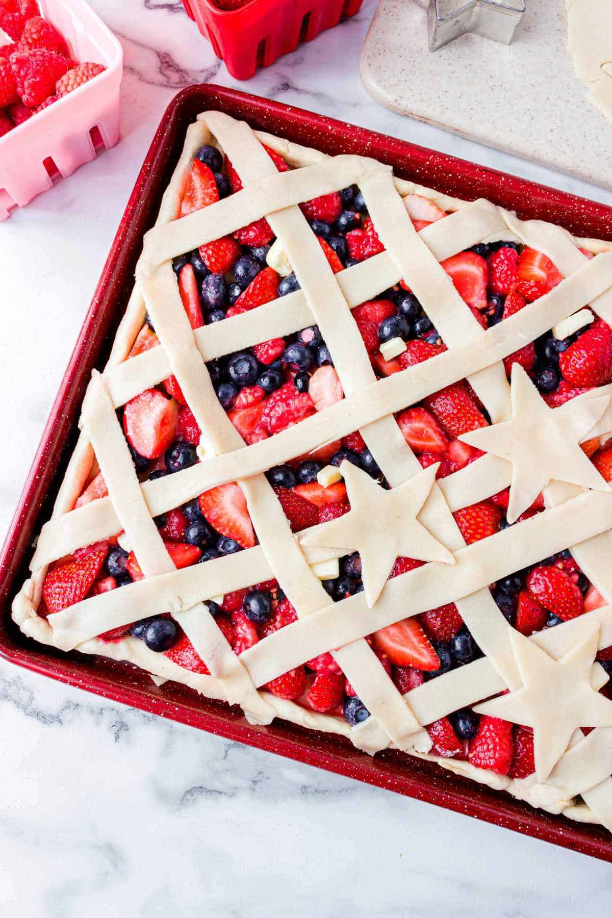unbaked sheet pan pie with crisscross lattice crust over strawberries, blueberries, and raspberries.